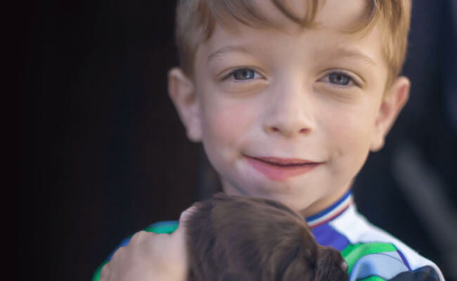 Kleiner Junge mit einer seltenen Stoffwechselerkrankung hält einen Welpen im Arm 